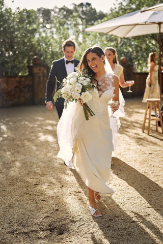 Bride holding white flowers, smiling, walking outside under sunlight