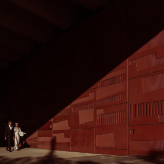 Couple walking beside a red geometric wall in shadow