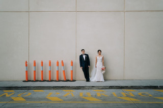 Bride and groom posing against a minimalist wall with no parking sign, by Todd and Alyda McGaw