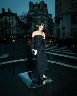 Model in a black gown standing on a reflective surface at an urban intersection